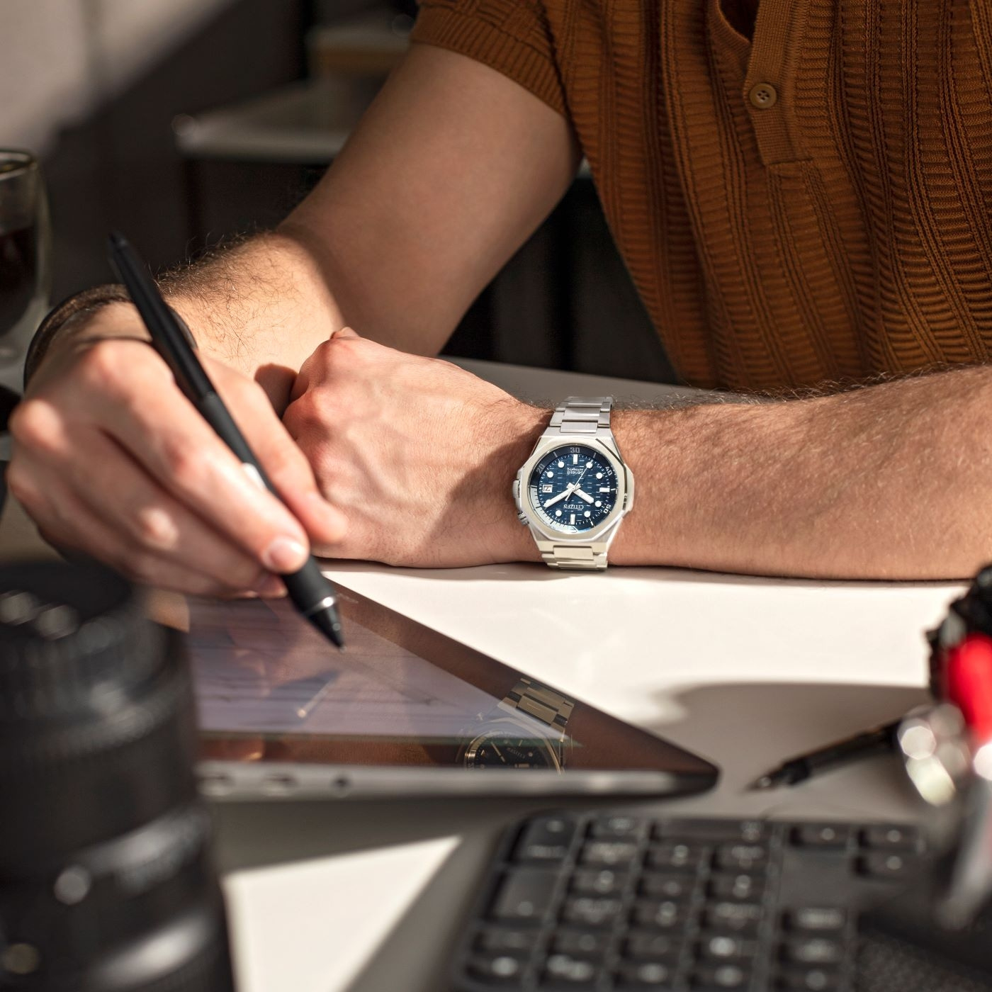 Mann arbeitet mit Tablet, trägt Uhr und schreibt mit einem Stift.
