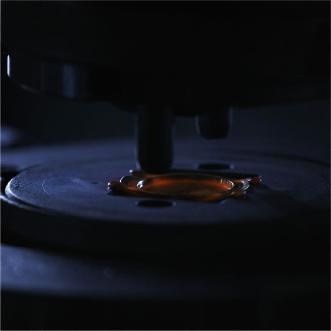 Nahaufnahme einer dunklen Maschine mit einem Tropfen oranger Flüssigkeit auf einer Platte.