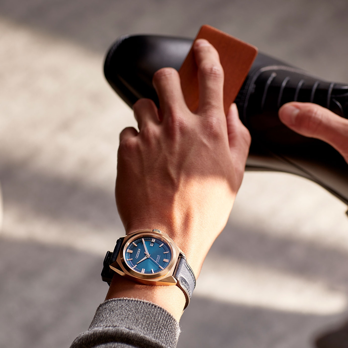 Mann poliert schwarzen Schuh, trägt goldene Uhr mit blauem Zifferblatt.