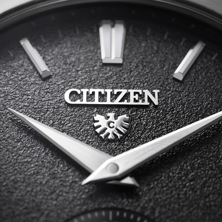 This close-up shows a Citizen watch's brushed silver case, textured white dial, and black leather strap connection.