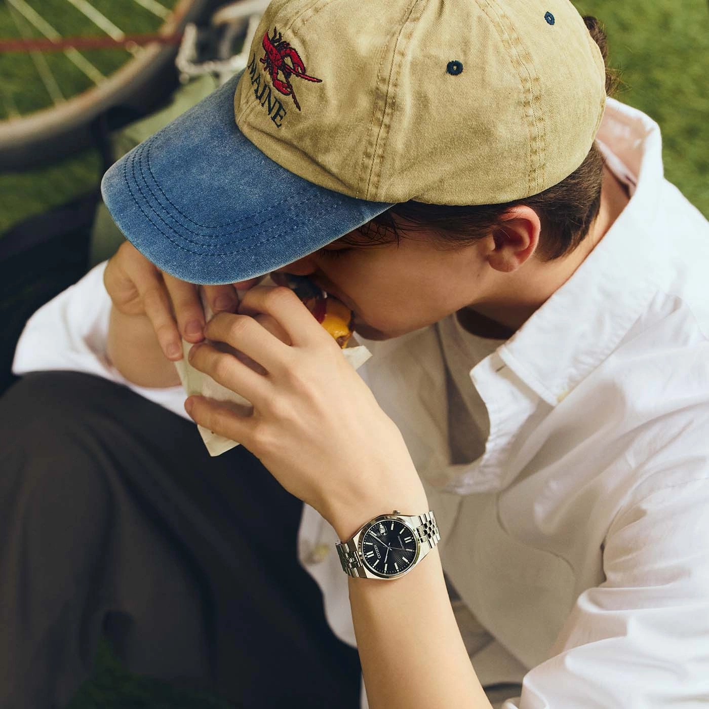 Eine Person isst einen Burger und trägt eine Baseballkappe und eine Uhr