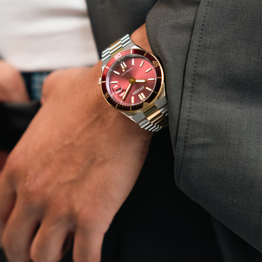 Ein Mann trägt eine rote Citizen Automatik-Uhr am Handgelenk, mit einem grauen Anzug.