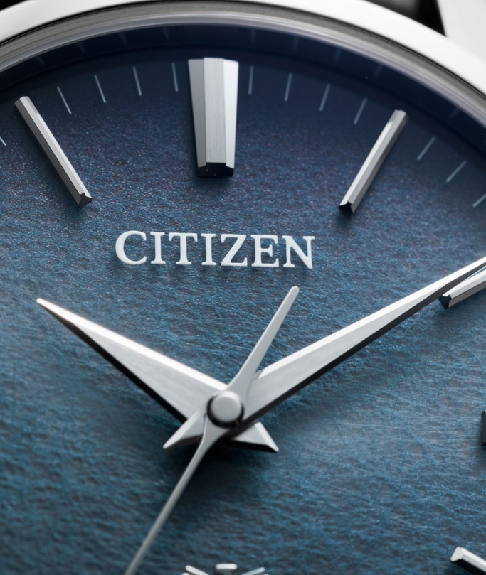 This close-up features a Citizen watch dial with a deep, textured blue surface. Polished silver-toned hour markers and hands are prominently displayed, alongside the "CITIZEN" logo, emphasizing the watch's sophisticated design and meticulous details.