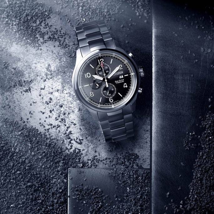 Citizen-Uhr auf strukturierter Oberfläche mit schwarzem Zifferblatt und Titan-Finish.