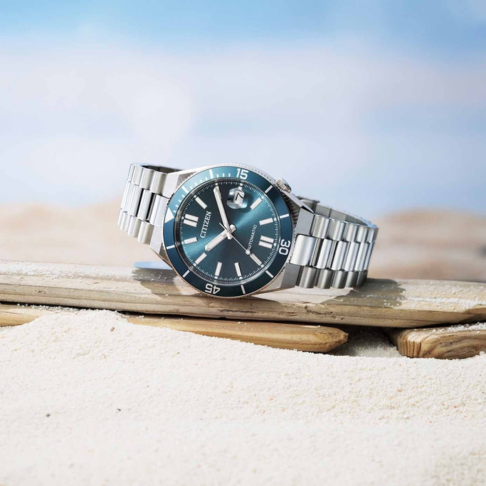 Eine Citizen Automatik-Uhr ruht auf Treibholz an einem Sandstrand.