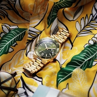 Eine goldene Citizen-Uhr auf einem gelben Blumenhemd.