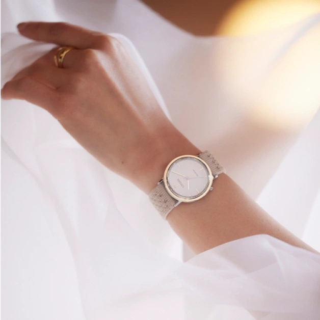 Nahaufnahme einer Armbanduhr mit beigem Armband am Handgelenk einer Frau.