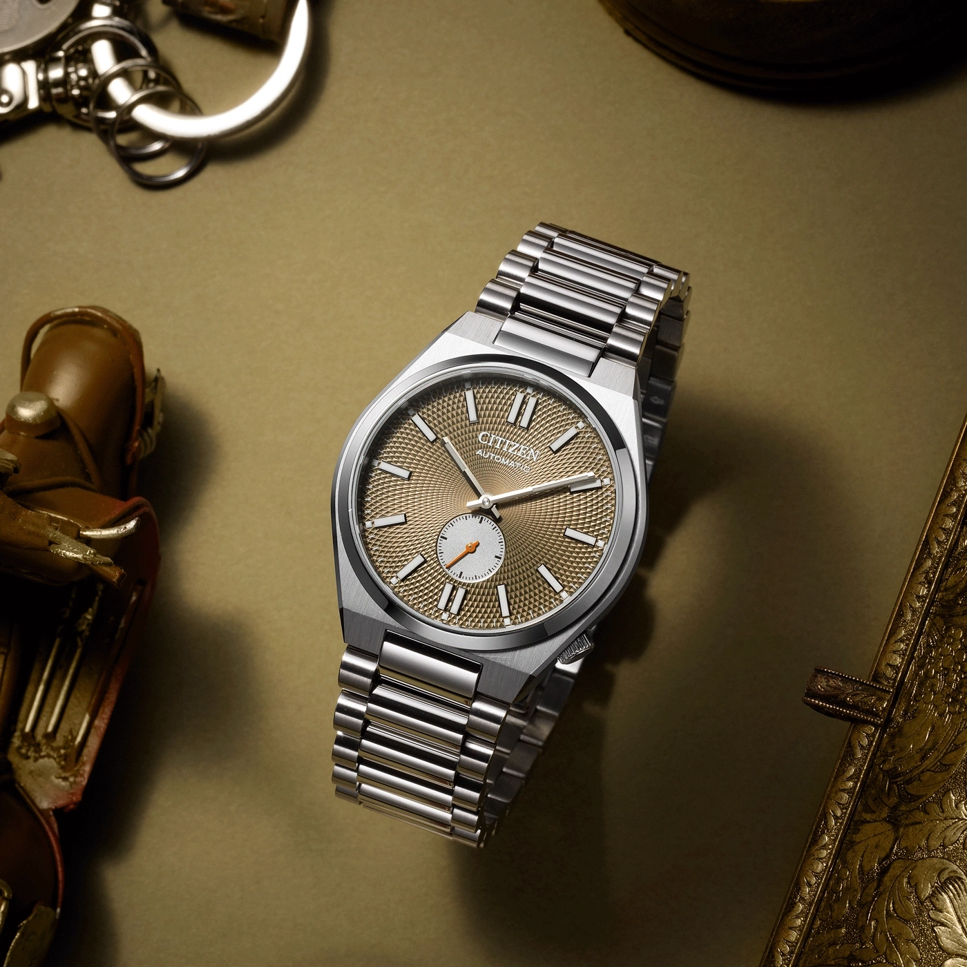 Citizen-Uhr mit silbernem Armband auf goldener Oberfläche mit Zubehör.