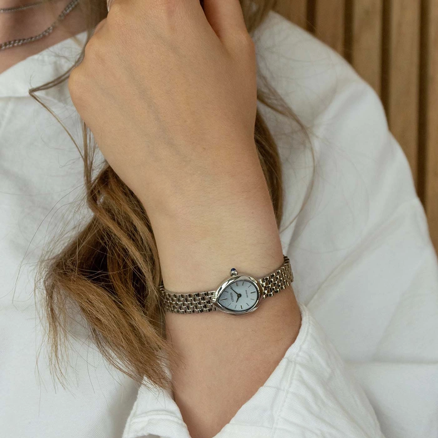 Frau trägt eine silberne Armbanduhr mit weißem Zifferblatt und blauen Stein.