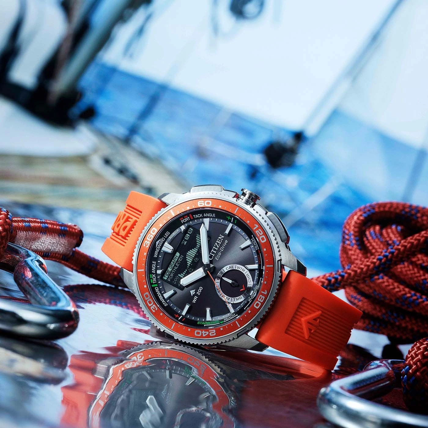 Nahaufnahme einer Citizen Eco-Drive Uhr mit orangefarbenem Armband, umgeben von Segelseilen und Karabinerhaken.