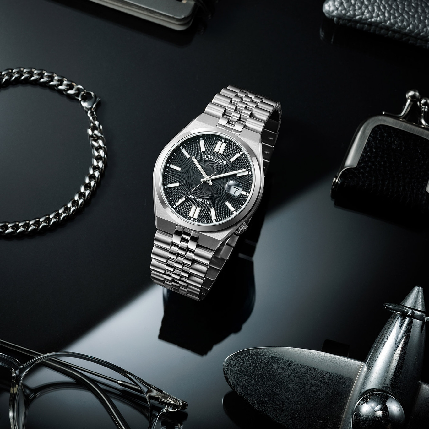 Citizen-Uhr mit Armband, Brille und Accessoires auf schwarzem Untergrund.