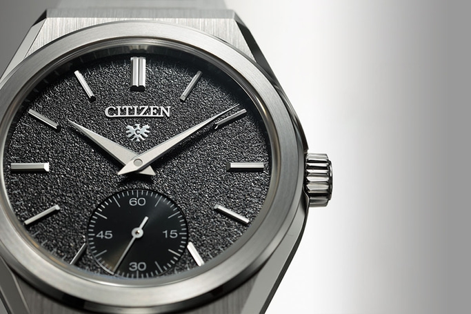 This close-up features a Citizen watch with a textured black dial and silver-toned case. It shows polished applied hour markers, sleek hands, and a sub-seconds dial at 6 o'clock, highlighting its sophisticated and precise design.