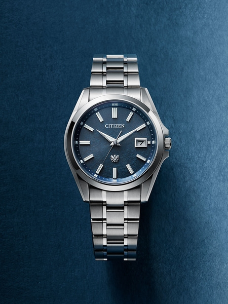 Citizen-Uhr mit blauem Zifferblatt und silbernem Armband auf blauem Hintergrund.