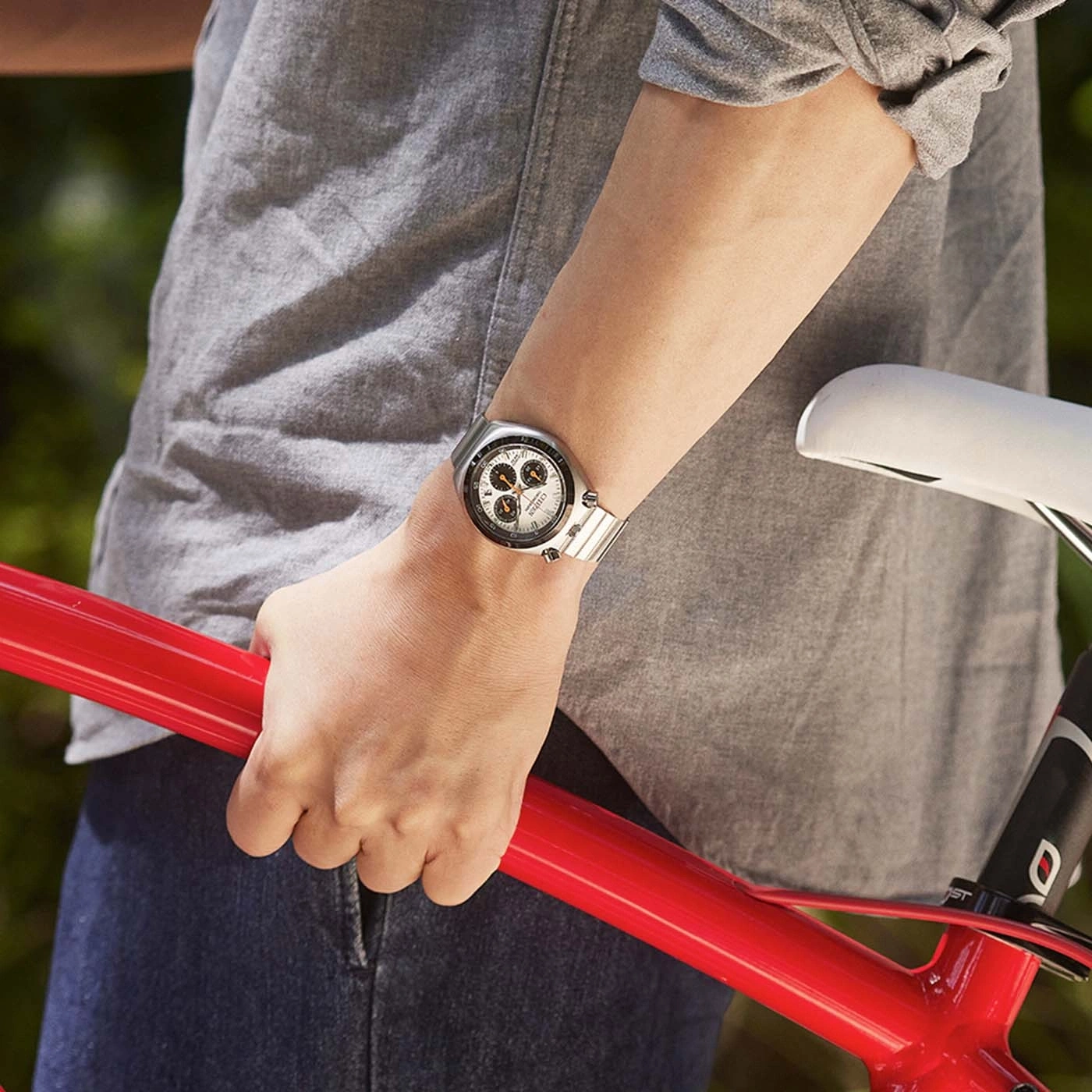 Person im grauen Hemd hält roten Fahrradrahmen, trägt eine Uhr.