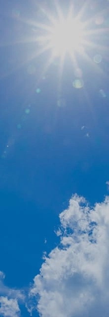 Helle Sonne am blauen Himmel mit ein paar flauschigen weißen Wolken.