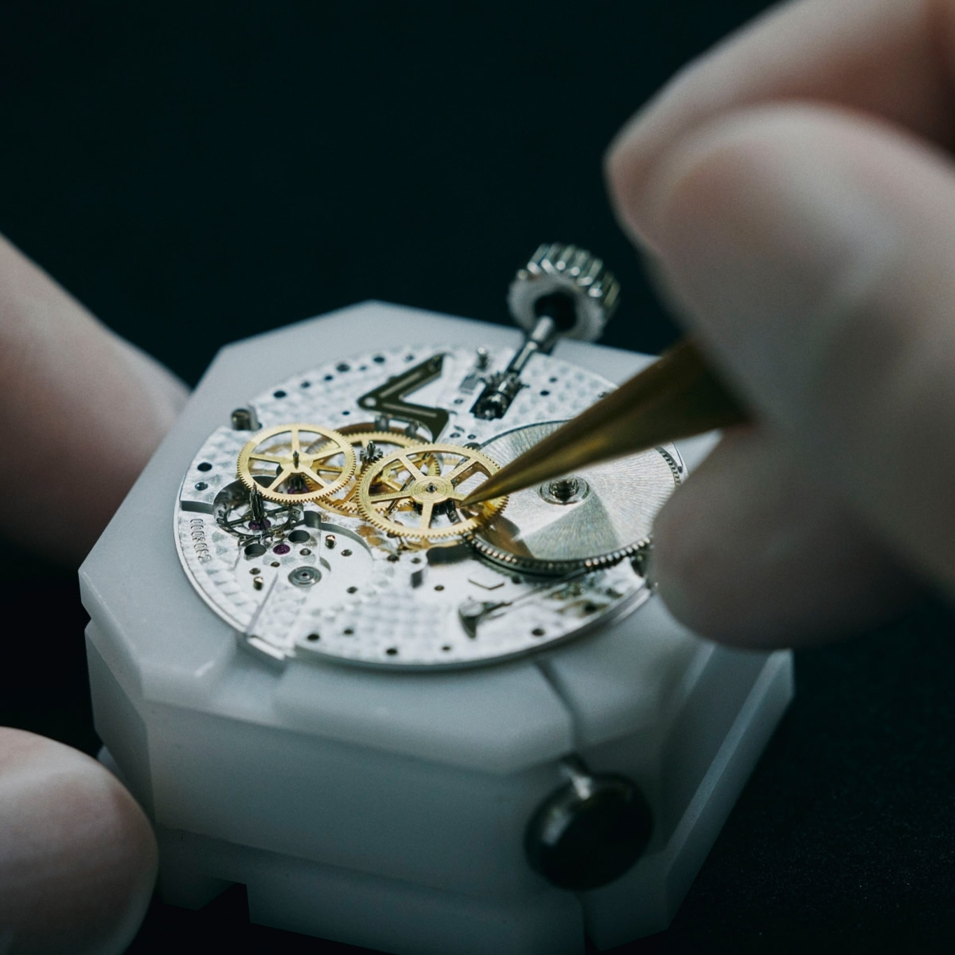 Nahaufnahme des Uhrwerks, das mit Pinzette und Händen zusammengebaut wird.
