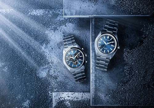 Zwei Citizen-Uhren mit blauen Zifferblättern auf dunklem Textur-Hintergrund.