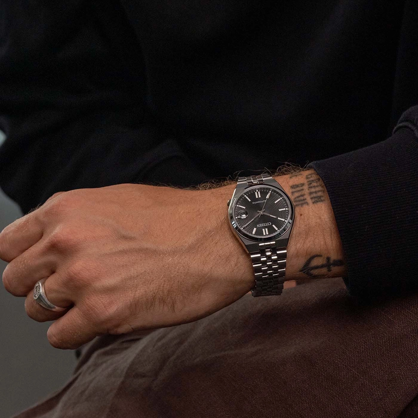 Mann trägt eine schwarze Citizen Automatik-Uhr mit silbernem Band und Ring.