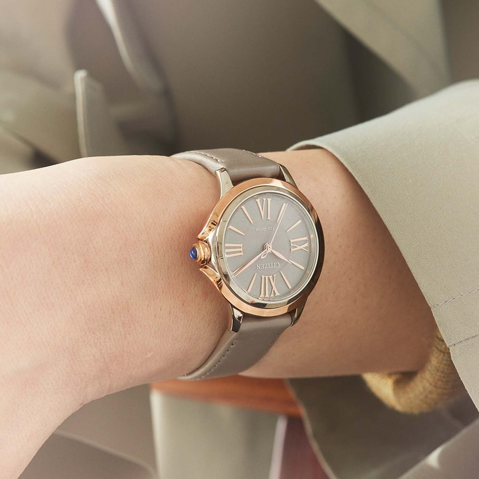 Nahaufnahme einer Citizen-Uhr am Handgelenk, mit grauem Armband und roségoldenen Akzenten.