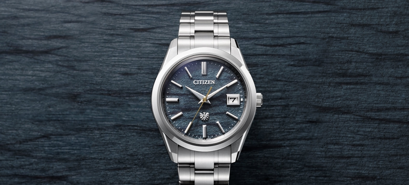A Citizen watch with a silver metal bracelet and textured blue dial is displayed on a dark, textured surface.