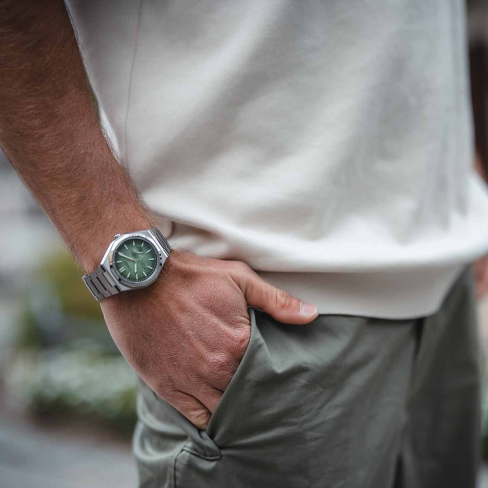 Mann trägt silberne Uhr mit grünem Zifferblatt, Hand in der Tasche.
