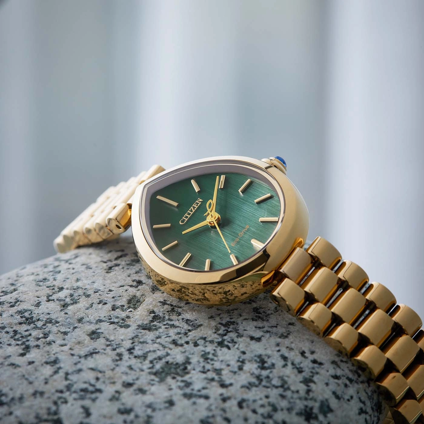 Eine goldene Citizen Eco-Drive Uhr mit grünem Zifferblatt ruht auf einem Stein.
