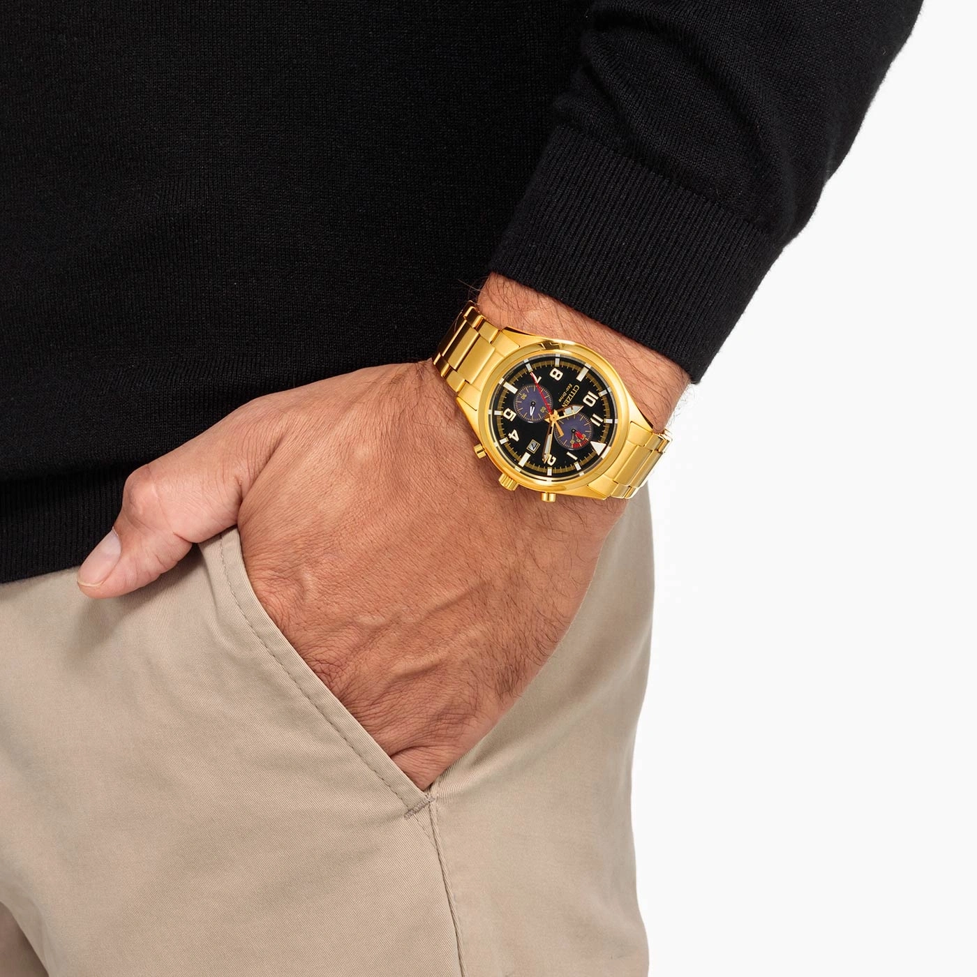 Mann mit goldener Uhr, schwarzem Pullover und beiger Hose.