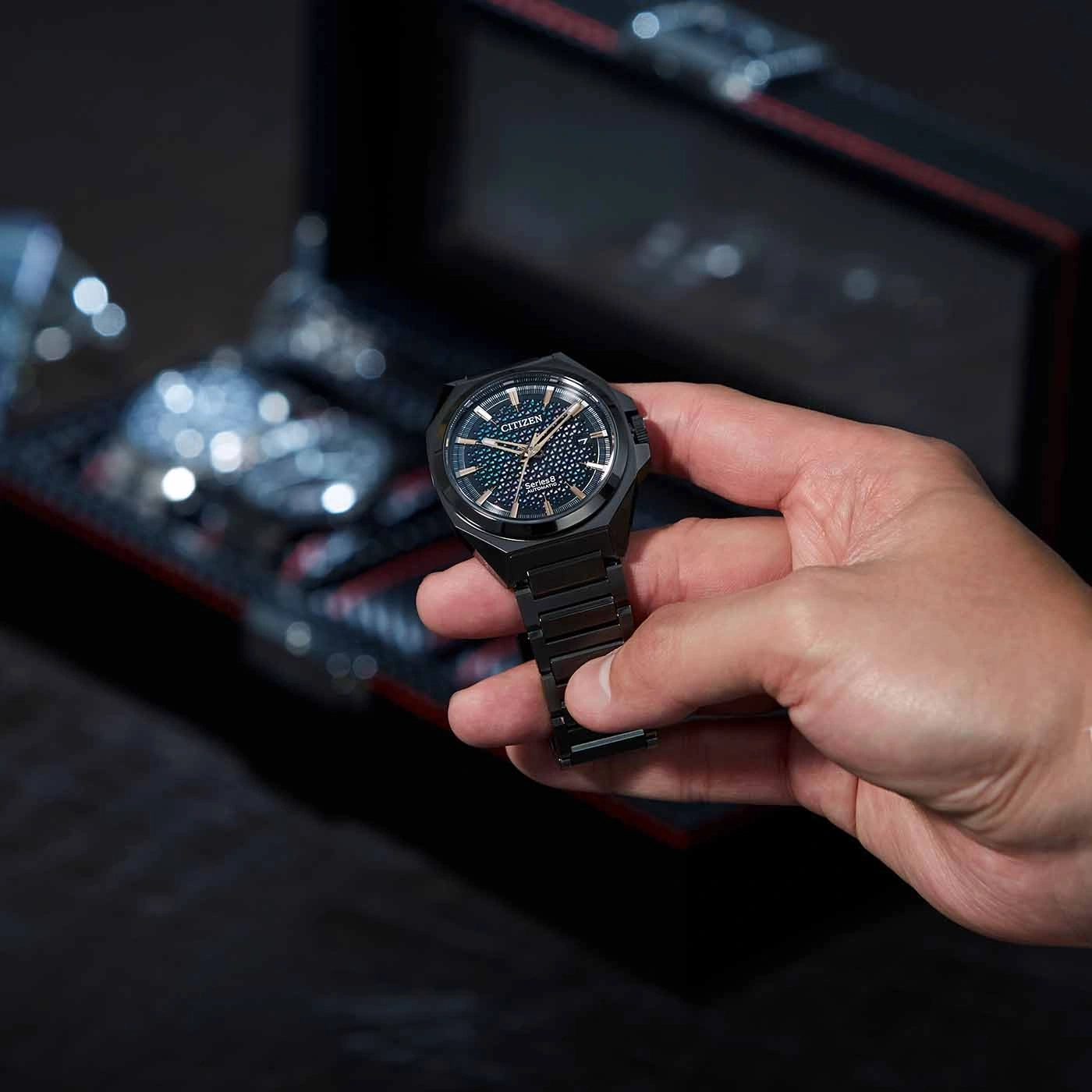 Eine Person hält eine schwarze Citizen-Uhr vor dunklem Hintergrund.