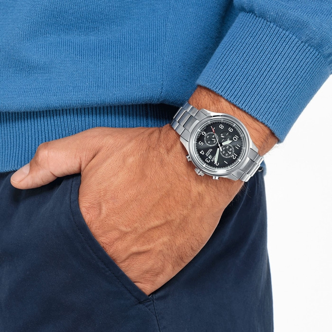 Mann mit Uhr, blauem Pullover und marineblauer Hose mit Hand in der Tasche.