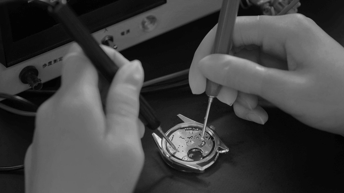 Hände, die mit Werkzeugen an einer Uhr arbeiten, Nahaufnahme, Schwarzweiß.