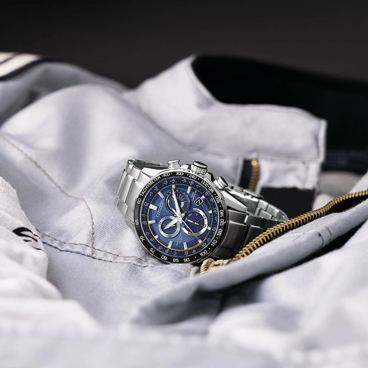 Citizen-Uhr auf grauer Jacke mit blauem Zifferblatt und silbernem Armband.