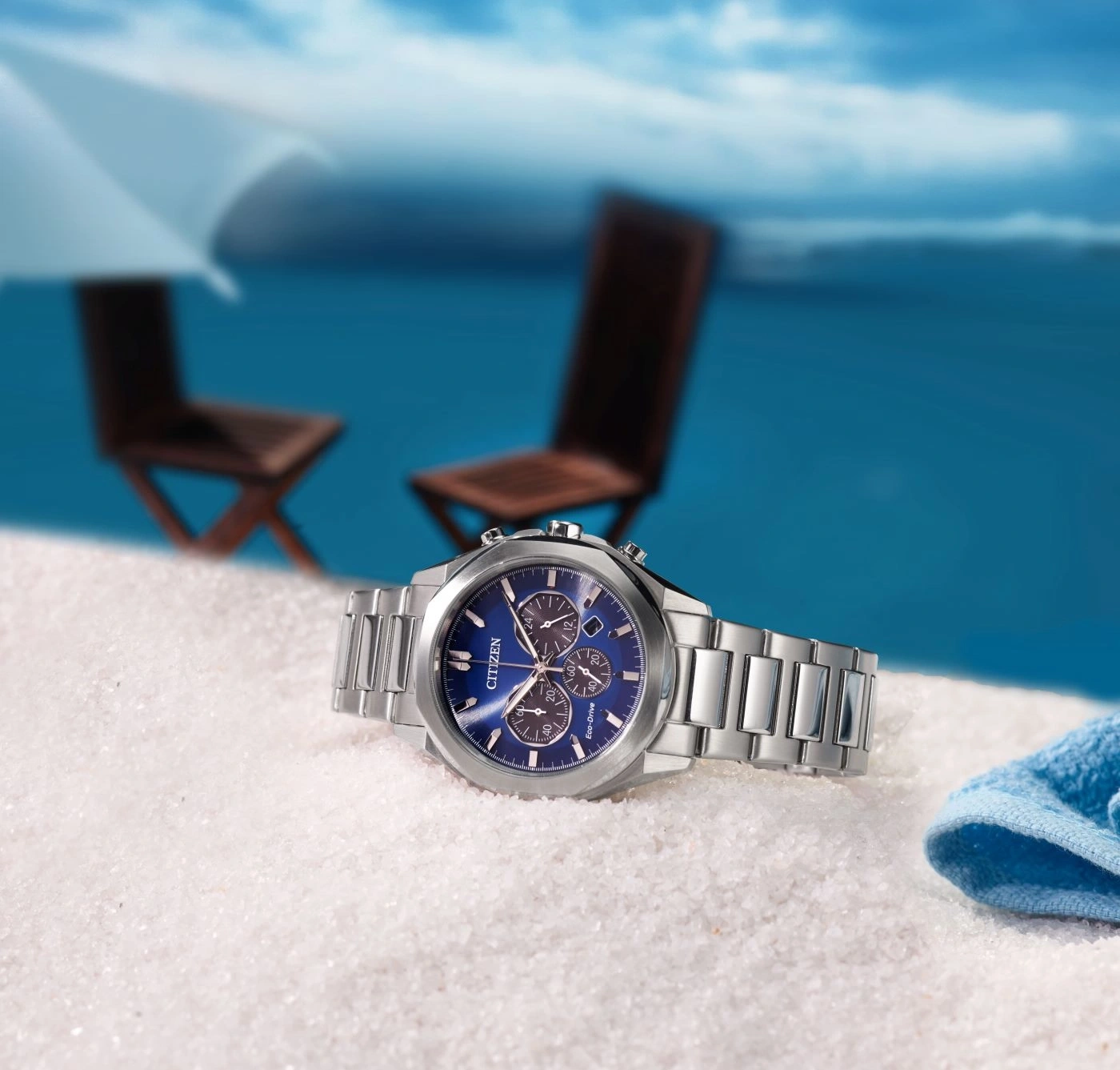 Citizen-Uhr auf Sand mit Strandhintergrund, blaues Zifferblatt und silbernes Armband