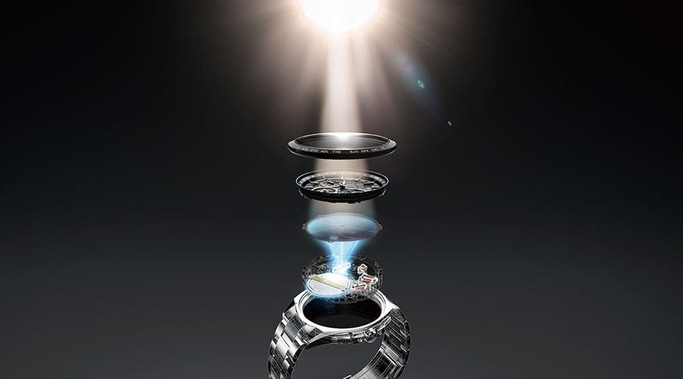 This image illustrates light-powered watch technology. A beam of light shines onto exploded layers, including the dial and components, before reaching a watch case, showing how light energy powers the timepiece.