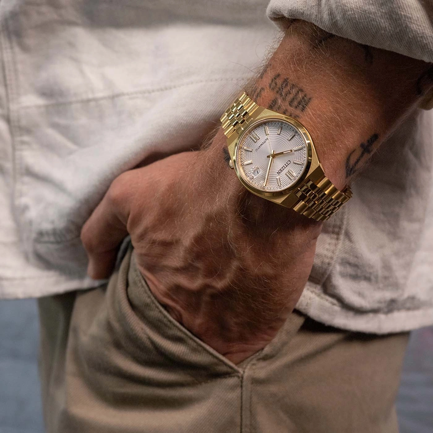 Goldene Uhr am Handgelenk eines Mannes mit Tattoos.