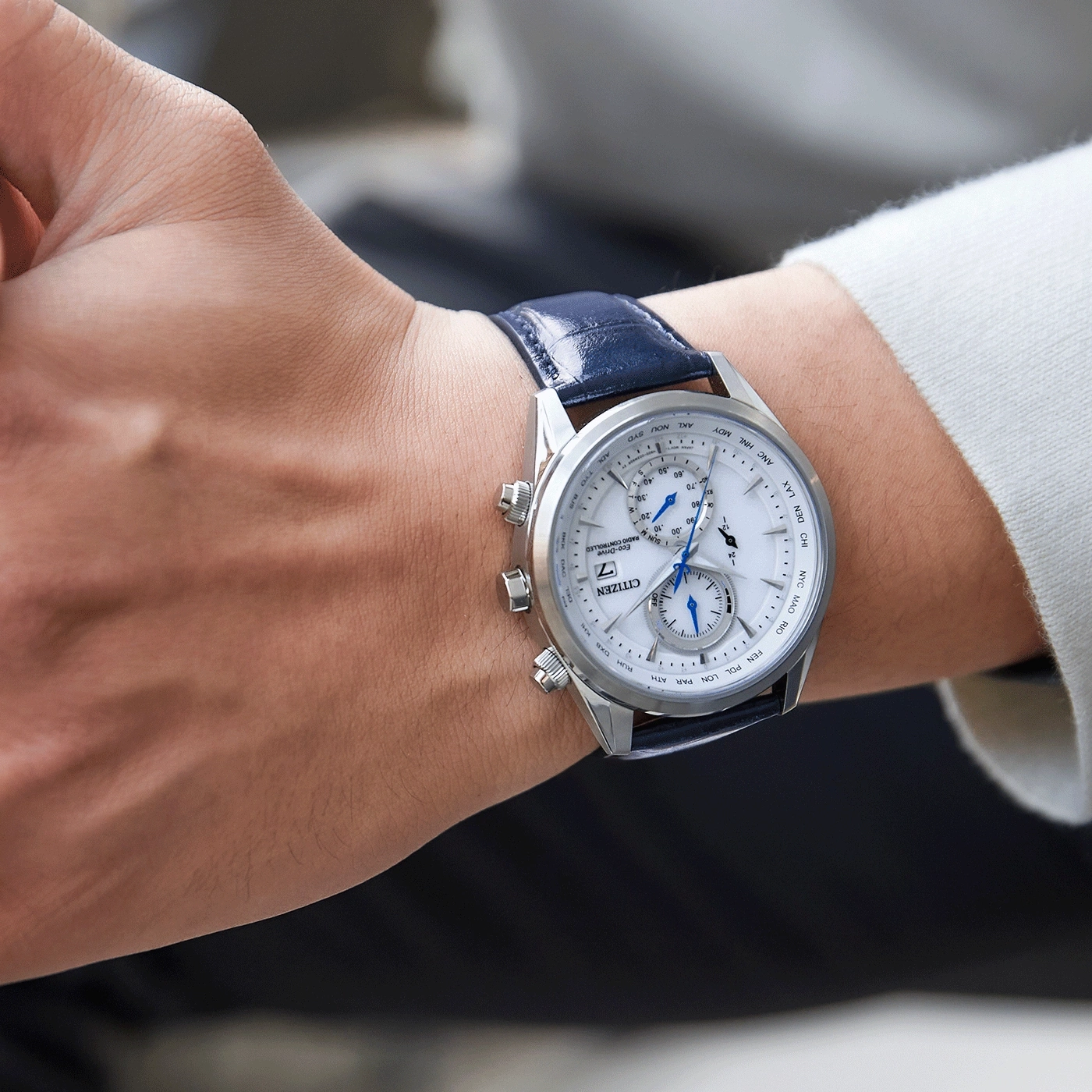 Nahaufnahme einer Citizen-Uhr am Handgelenk, blaues Lederarmband, weißes Zifferblatt, silbernes Gehäuse.