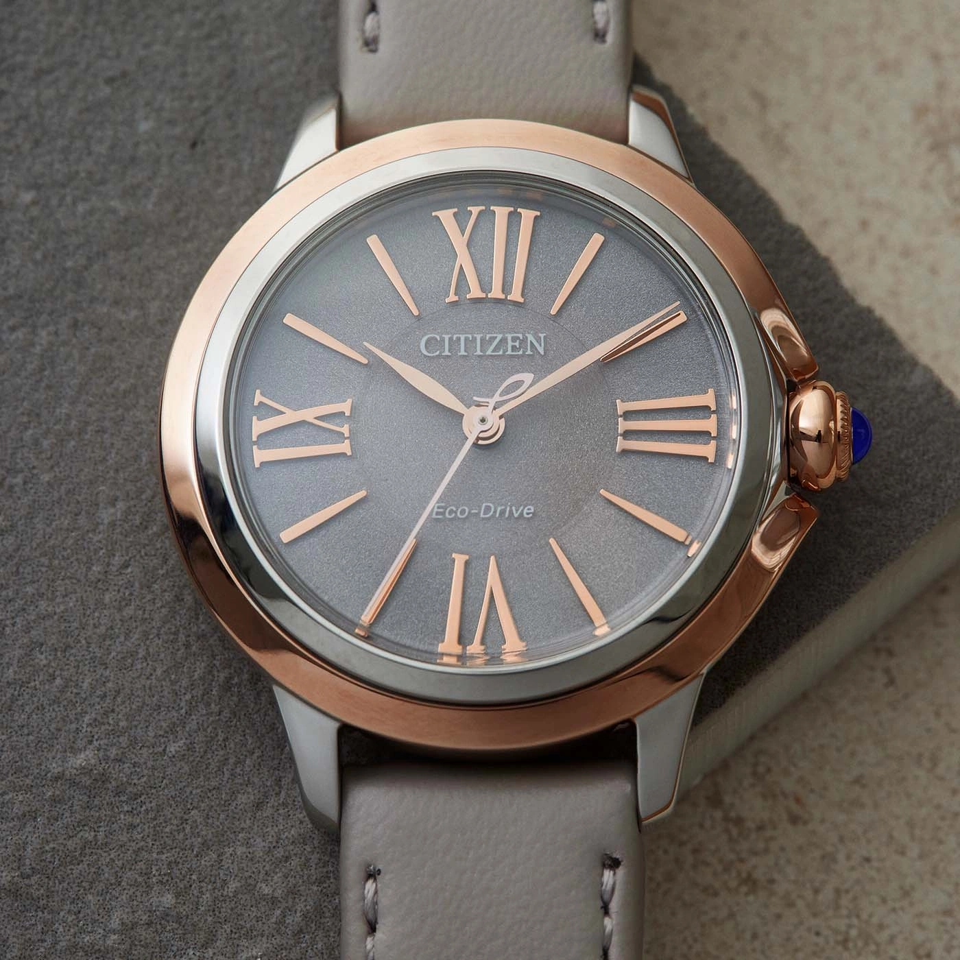 Citizen-Uhr mit grauem Zifferblatt, roségoldenen Akzenten und grauem Lederarmband.