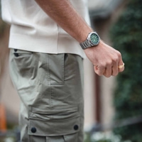 Mann mit Uhr und Ring, mit grünem Zifferblatt und khakifarbener Hose.