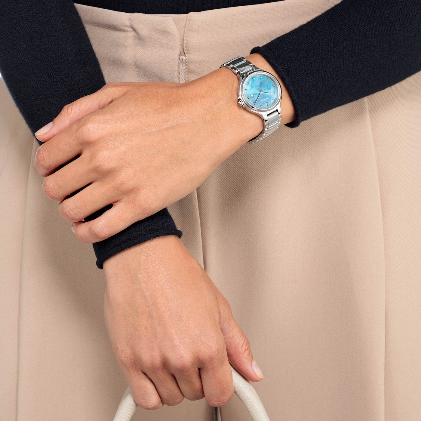 Frau mit silberner Uhr und blauem Zifferblatt, hält eine weiße Tasche.