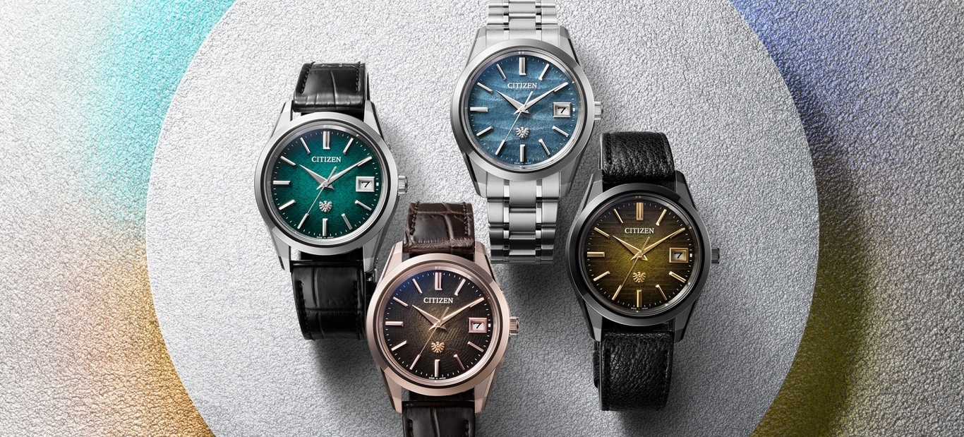 Vier Citizen-Uhren mit verschiedenfarbigen Zifferblättern und Armbändern auf strukturiertem Hintergrund.