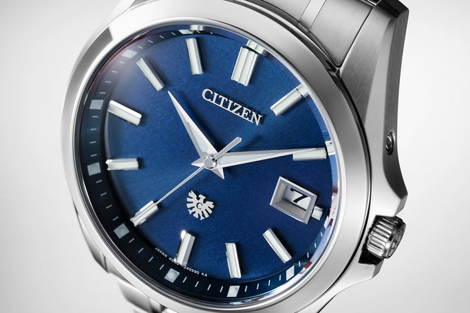 This close-up showcases a sophisticated Citizen watch with a vibrant blue, textured dial. It features polished silver-toned hands and applied hour markers, a date window at 3 o'clock, and the Citizen logo with an eagle emblem, highlighting its elegant de