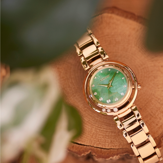 Goldene Citizen-Uhr mit grünem Zifferblatt und Diamanten auf Holzoberfläche.