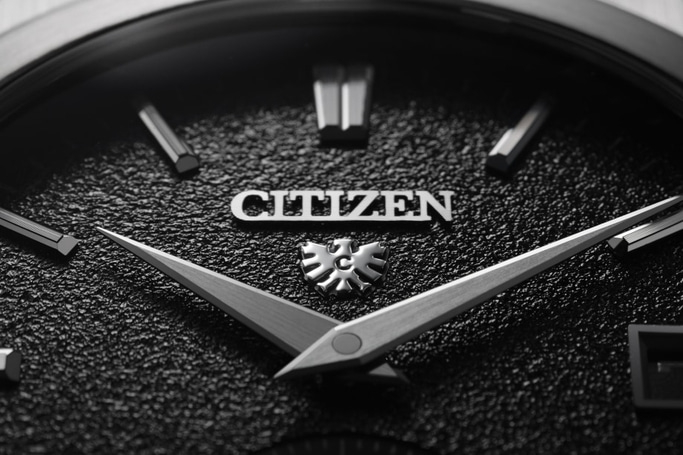 This image shows a close-up of a Citizen watch dial. It features a deep green, textured face with polished silver-toned hands and applied indices. A date window is at 3 o'clock, with the Citizen logo and eagle emblem above.