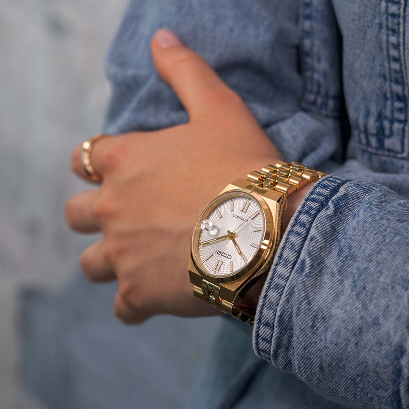 Goldene Citizen-Uhr am Handgelenk in einer Jeansjacke.