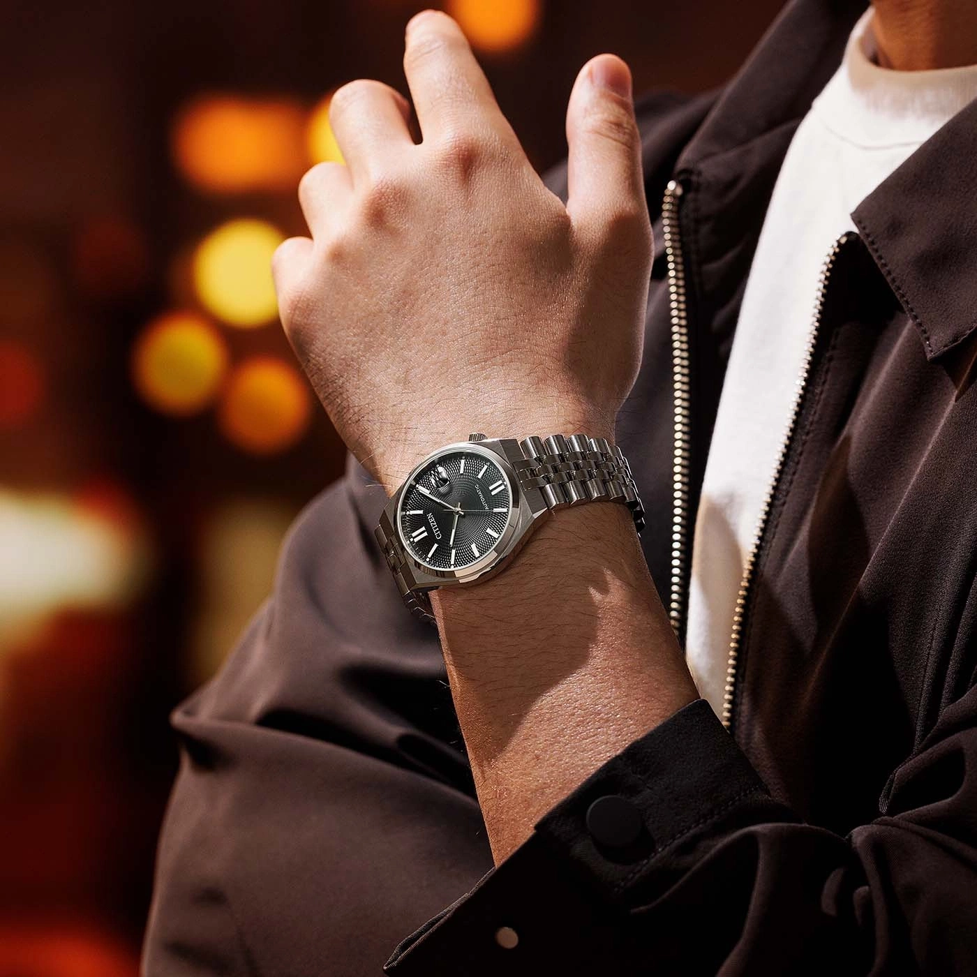 Mann trägt silberne Uhr mit schwarzem Zifferblatt und brauner Jacke.