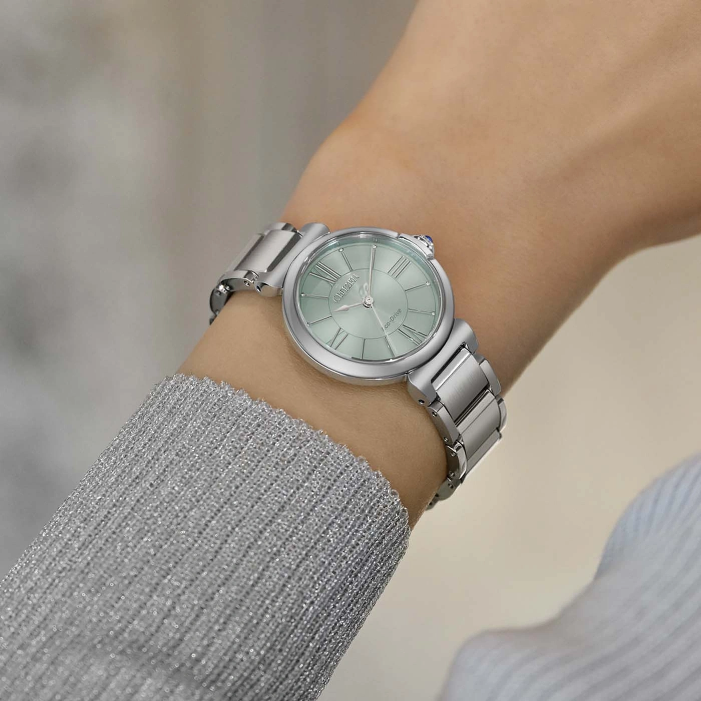 Das Handgelenk einer Frau mit einer silbernen Uhr mit hellgrünem Zifferblatt.