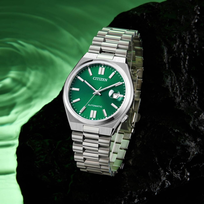 Citizen-Uhr mit grünem Zifferblatt und silbernem Armband auf dunkler Oberfläche.