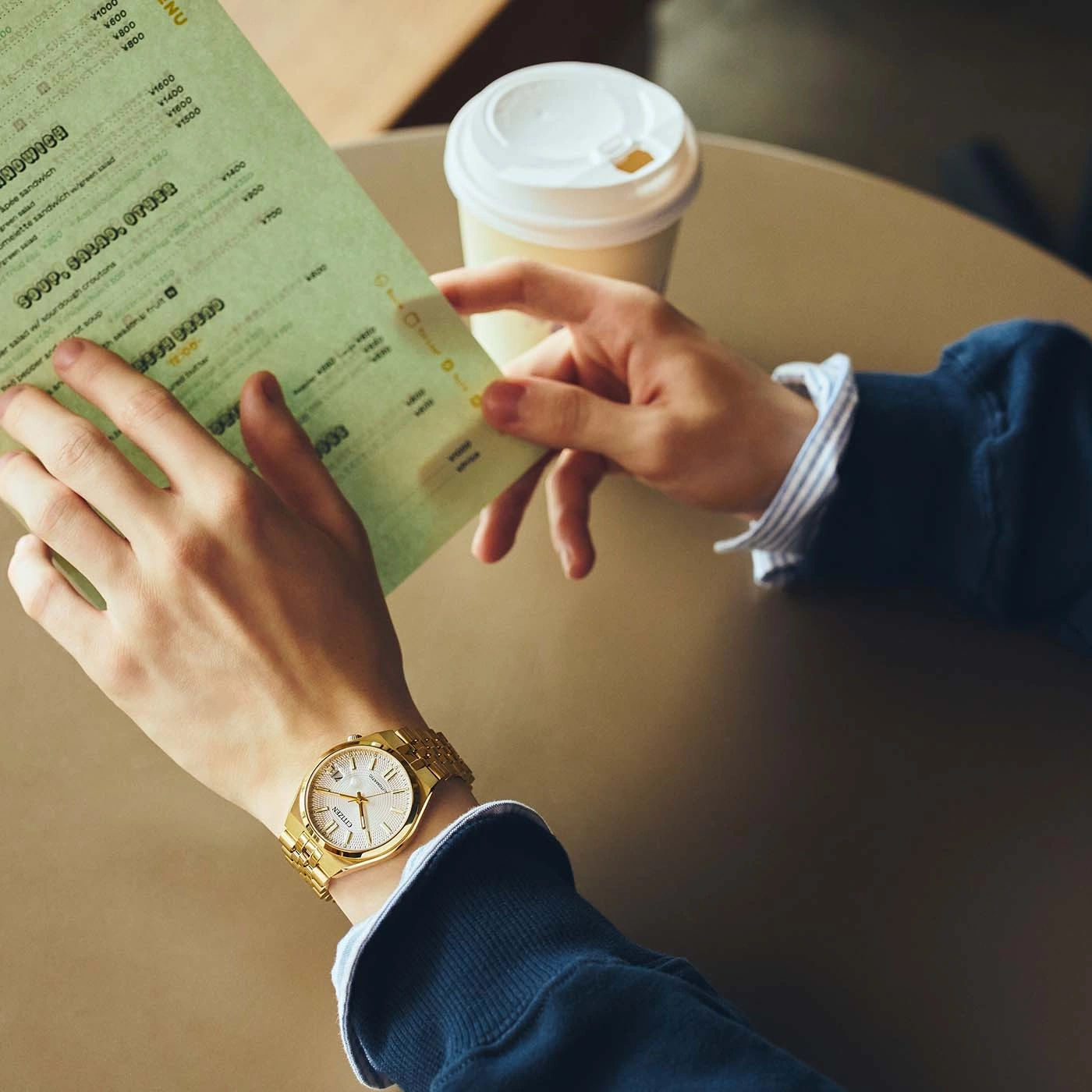 Eine Person betrachtet eine Speisekarte und hält eine Kaffeetasse.