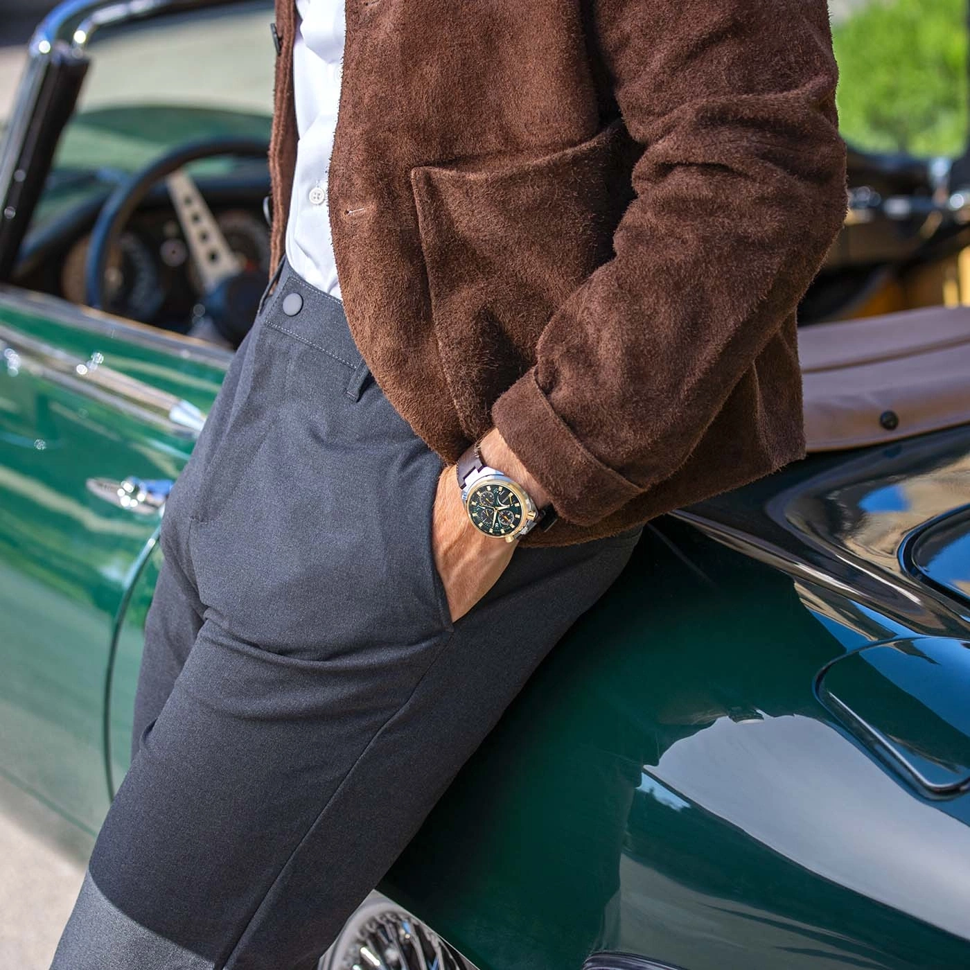 Mann lehnt an einem alten grünen Auto, trägt braune Jacke und Uhr.
