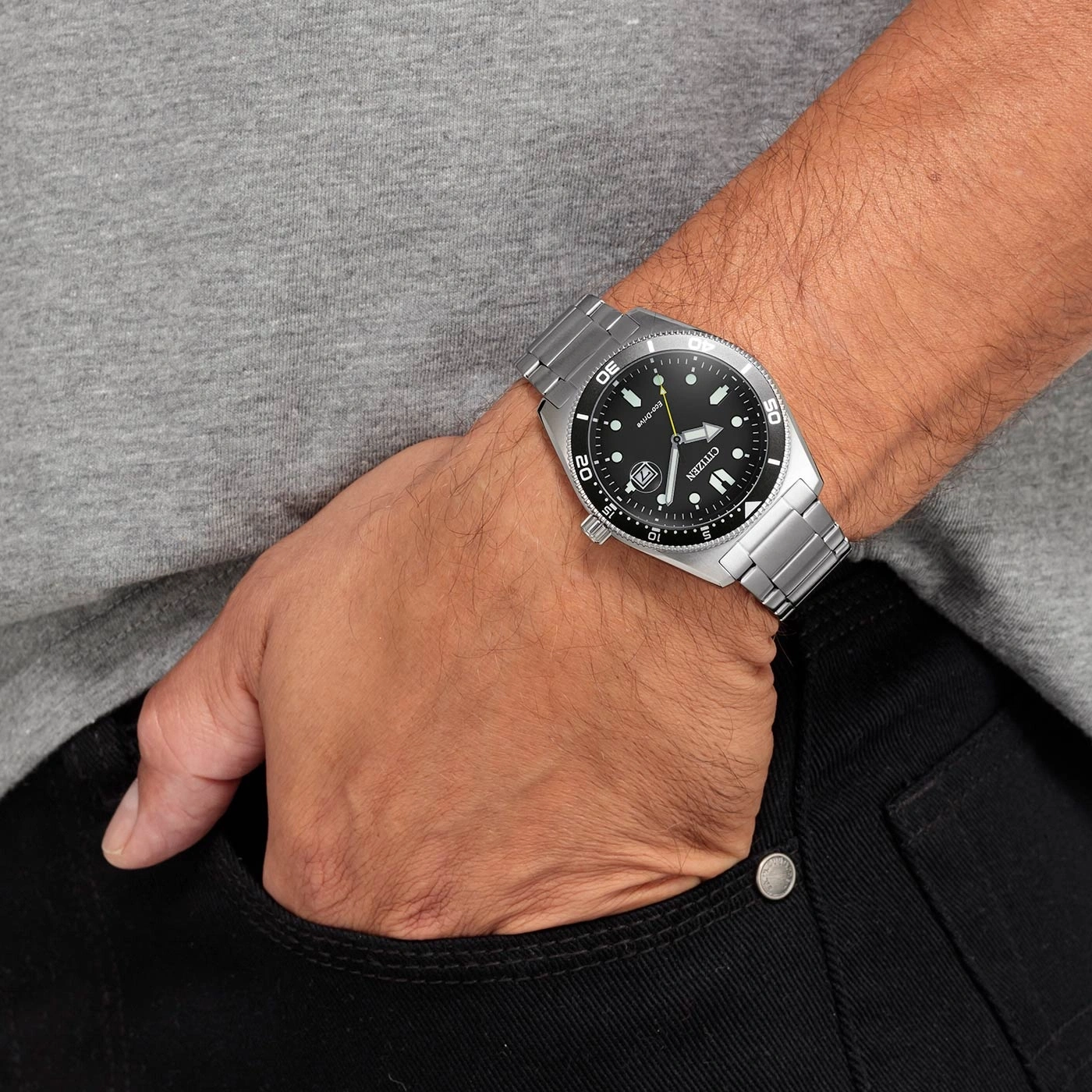 Mann mit Citizen-Uhr, Hand in der Tasche, schwarze Jeans, graues Hemd.