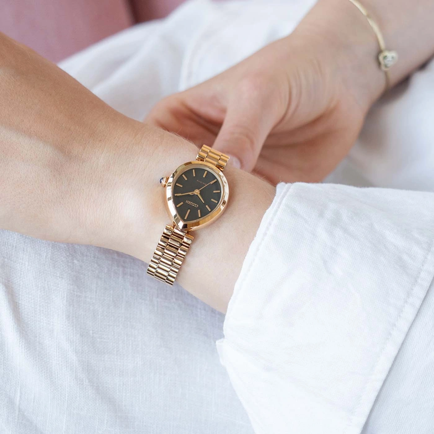 Das Handgelenk einer Frau trägt eine goldene Citizen-Uhr und ein Armband.